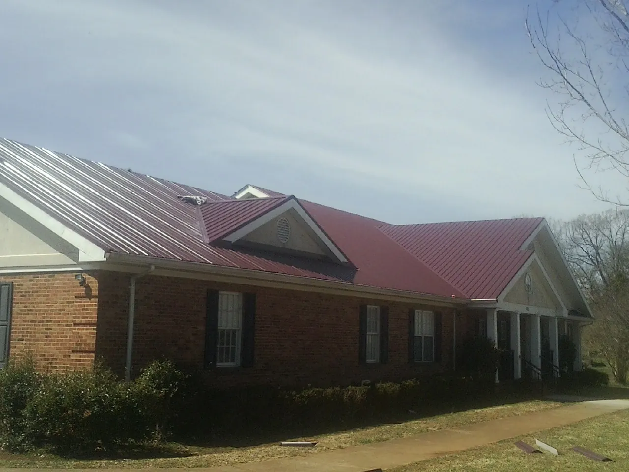 Red metal roof with gabled entries on a long brick building, from a Hail Damage Roof Repair job in Scott Bar