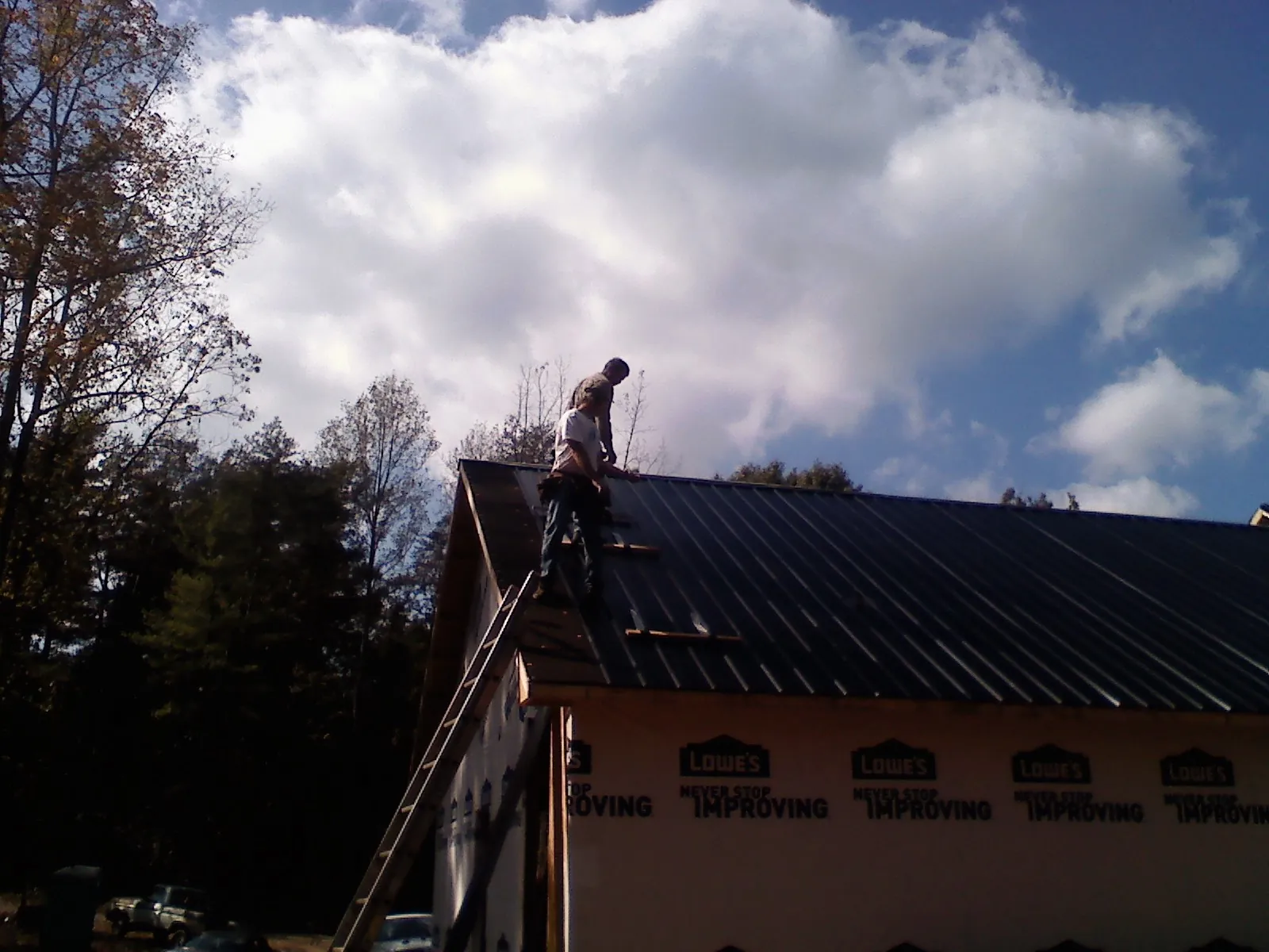 Roofer fastening dark metal panels high against a cloudy sky, from a Roof Inspection job in Scott Bar